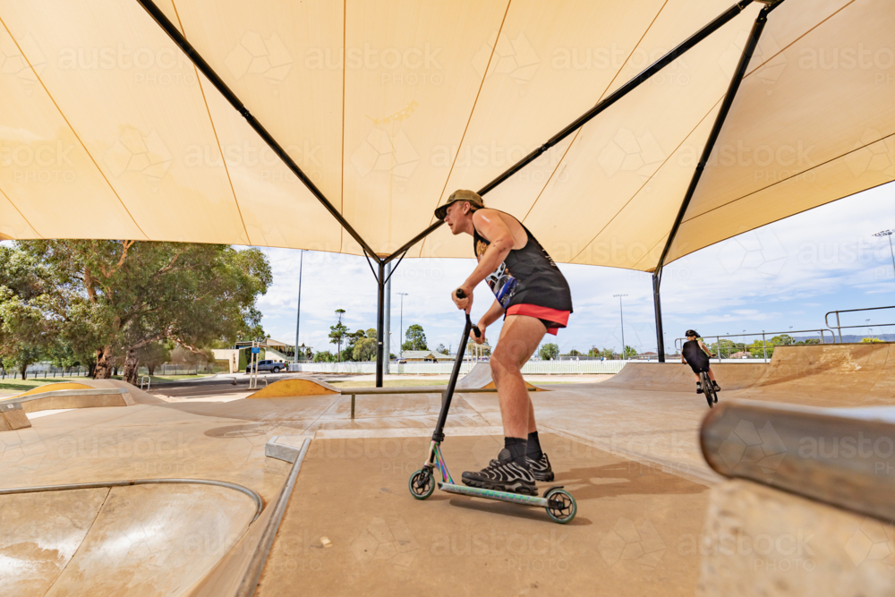 Image of Teen boy riding scooter on ramps at skate park focus on ...