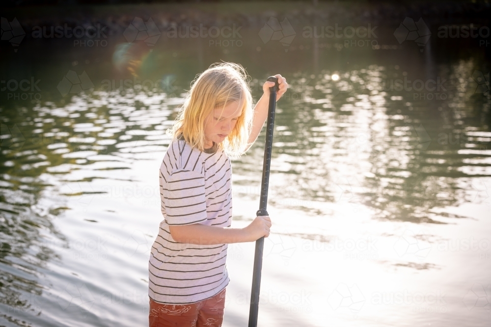 Teen boy riding stand up paddle board in golden afternoon light - Australian Stock Image