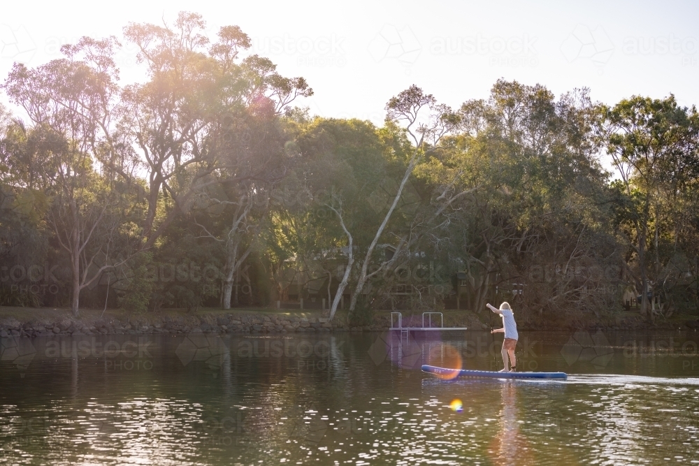 Teen boy riding stand up paddle board in golden afternoon light - Australian Stock Image