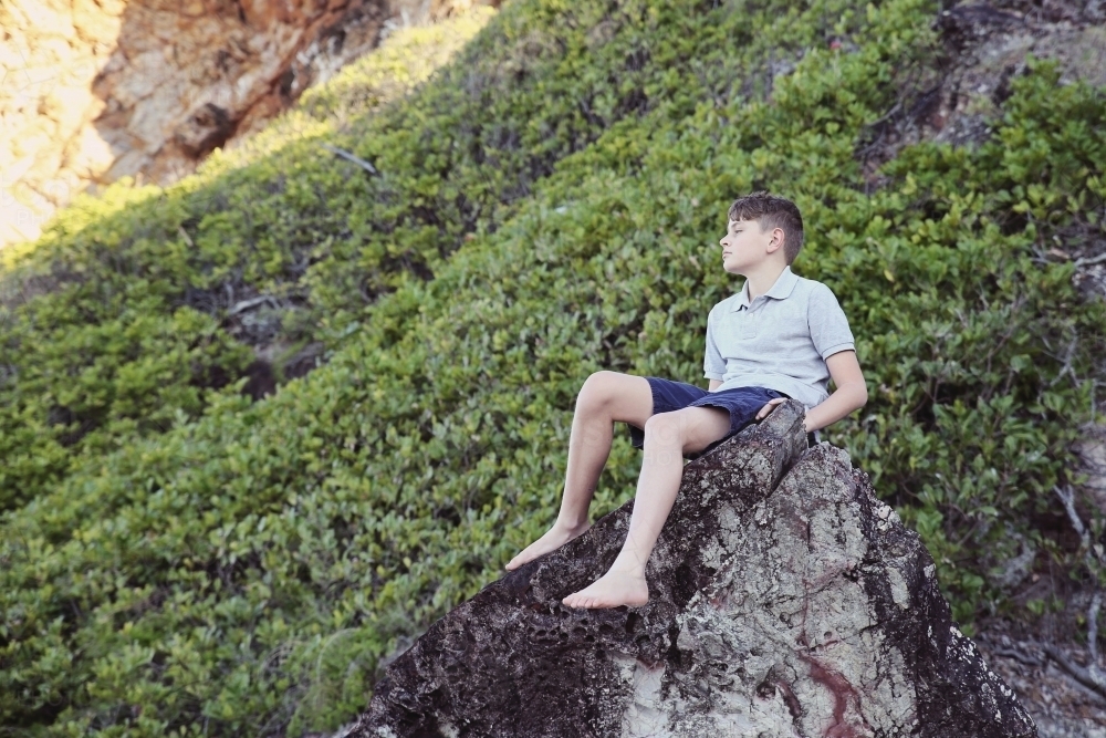 Image of Teen boy sitting alone on rock - Austockphoto