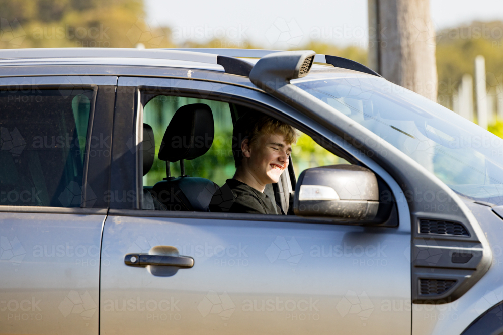 Teen boy sitting in car smiling at vineyard - Australian Stock Image