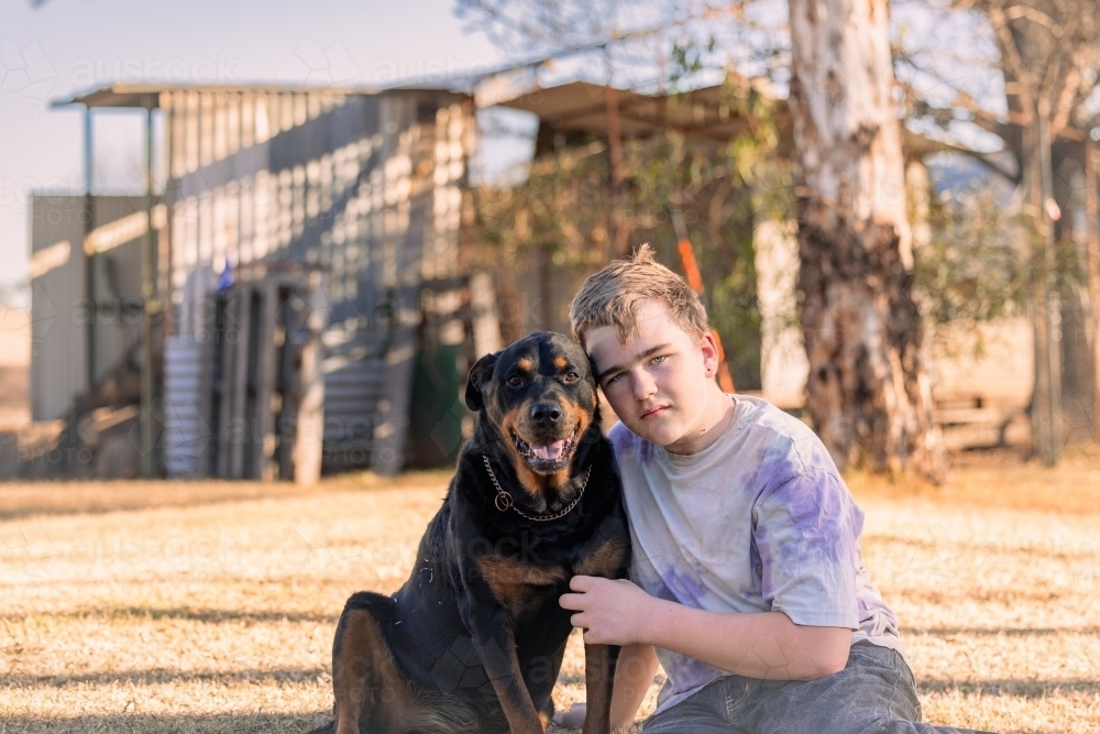 Teen boy sitting on grass with pet Rottweiler dog - Australian Stock Image