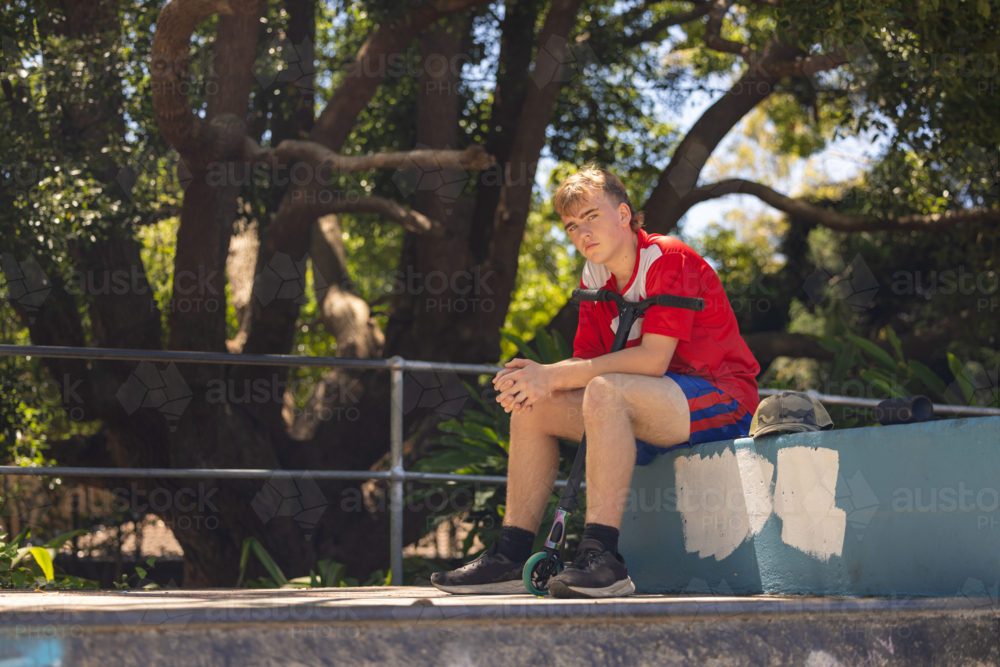 Image of Teen boy sitting with scooter at skate park - Austockphoto