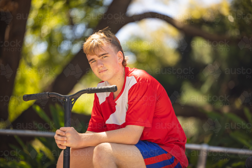 Image of Teen boy sitting with scooter at skate park - Austockphoto