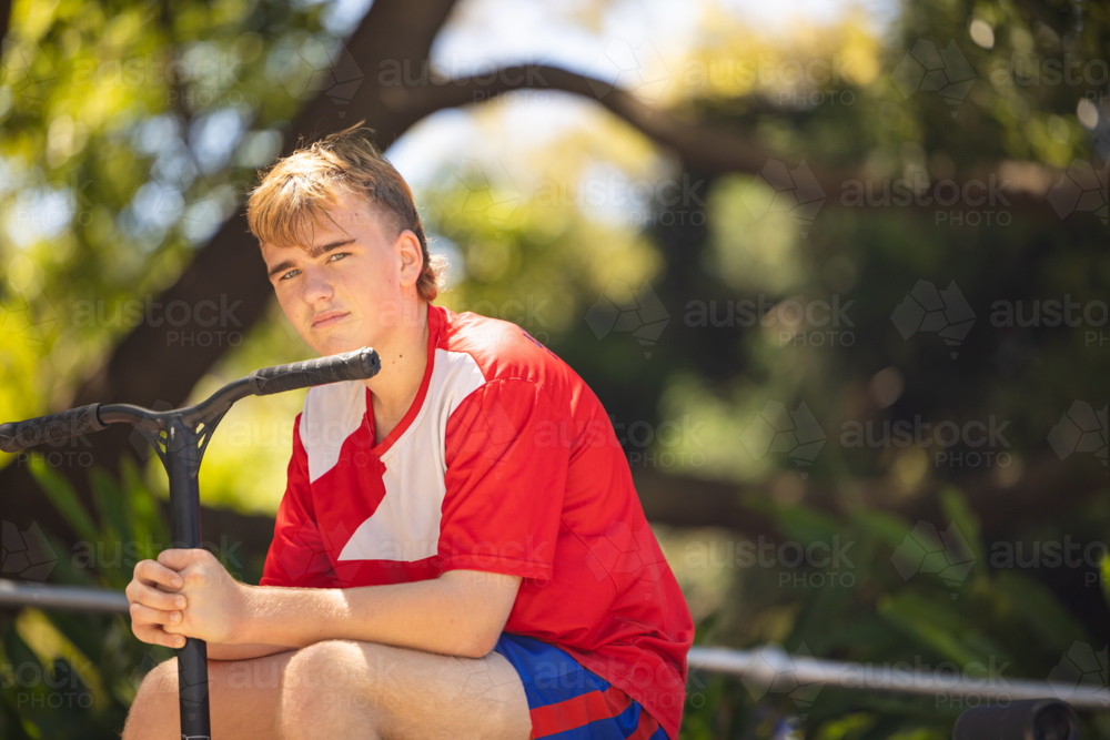 Teen boy sitting with scooter at skate park - Australian Stock Image