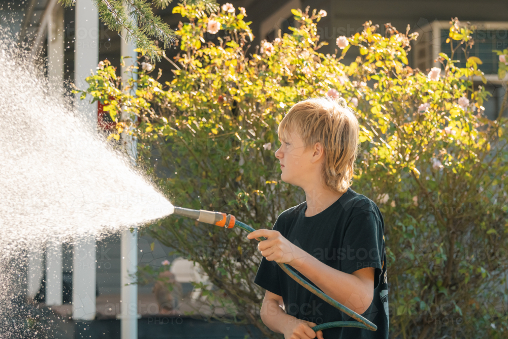 Teen boy spraying hose in yard at home - Australian Stock Image