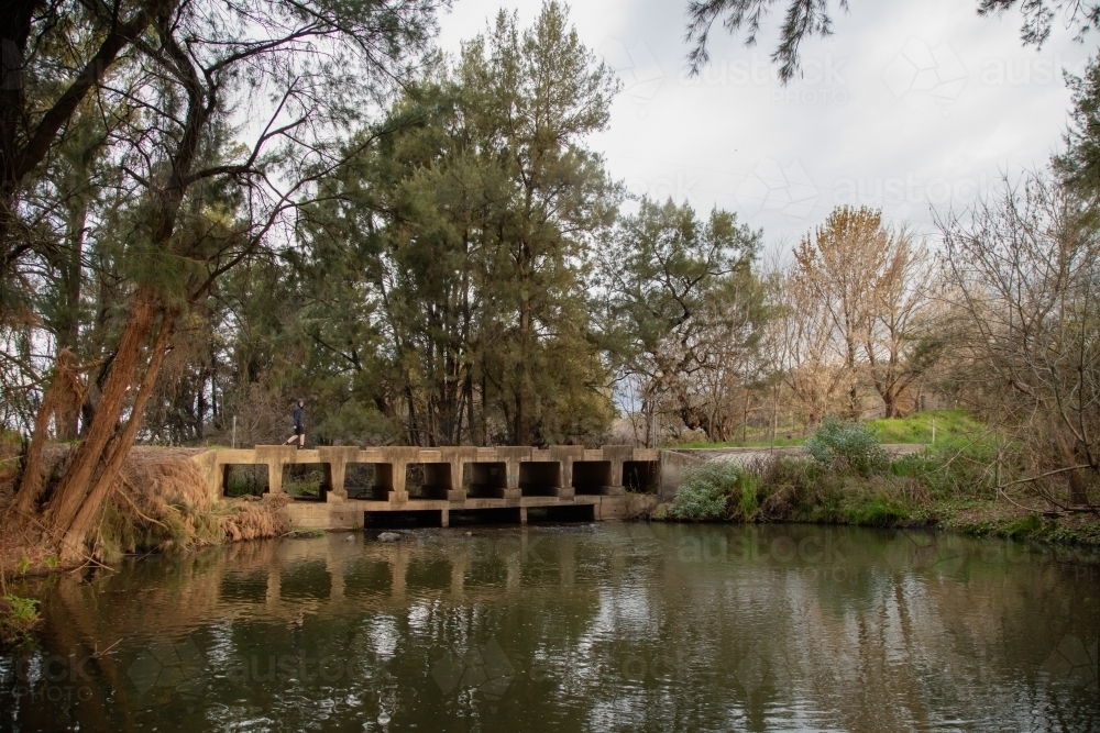 Teen boy walking across low bridge over the Cudgegong River in rural New South Wales - Australian Stock Image