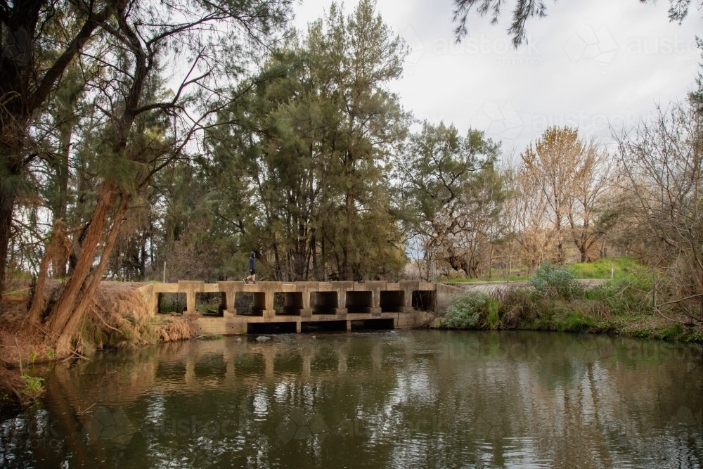 Teen boy walking across low bridge over the Cudgegong River in rural New South Wales - Australian Stock Image