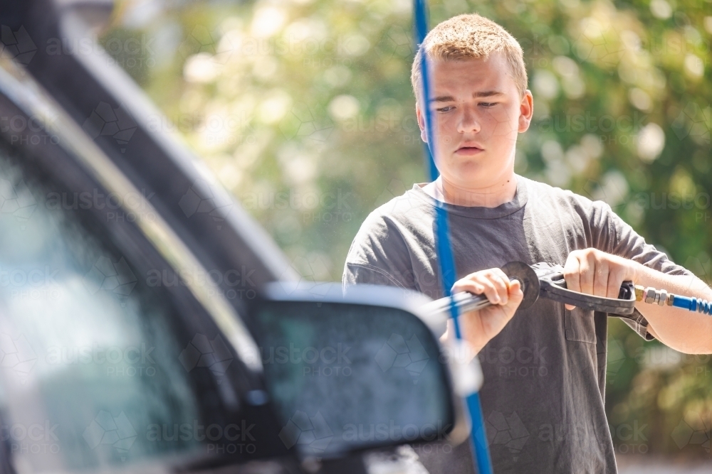 Teen boy washing vehicle in self-service car wash bay - Australian Stock Image