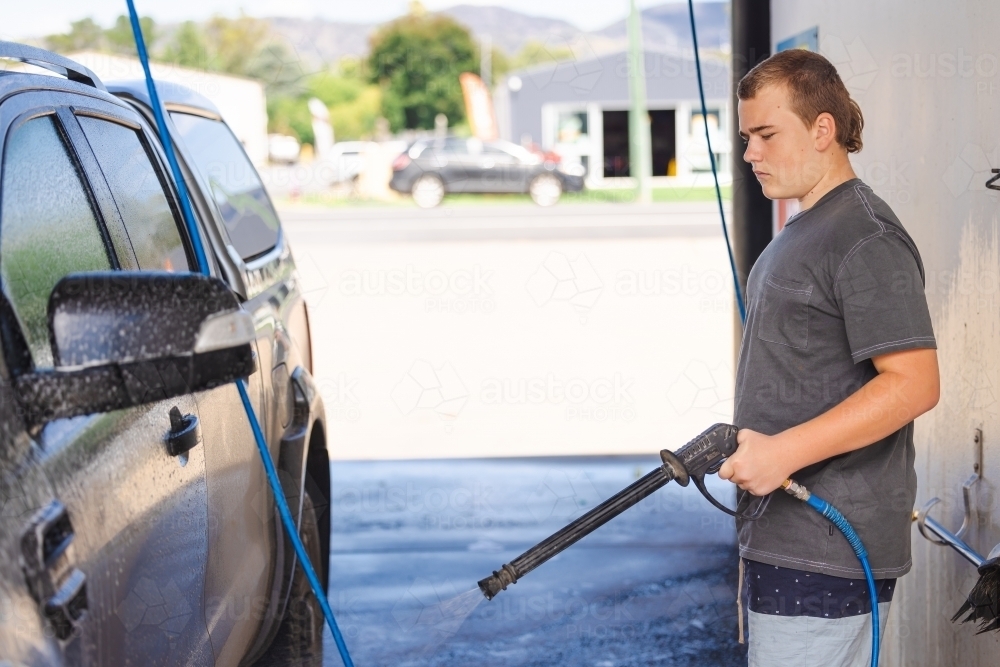 Teen boy washing vehicle in self-service car wash bay - Australian Stock Image