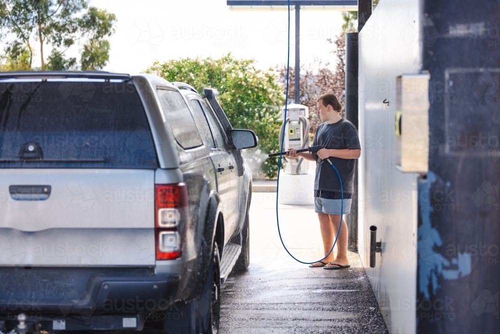 Teen boy washing vehicle in self-service car wash bay - Australian Stock Image