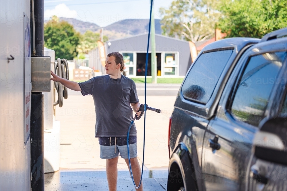 Teen boy washing vehicle in self-service car wash bay - Australian Stock Image