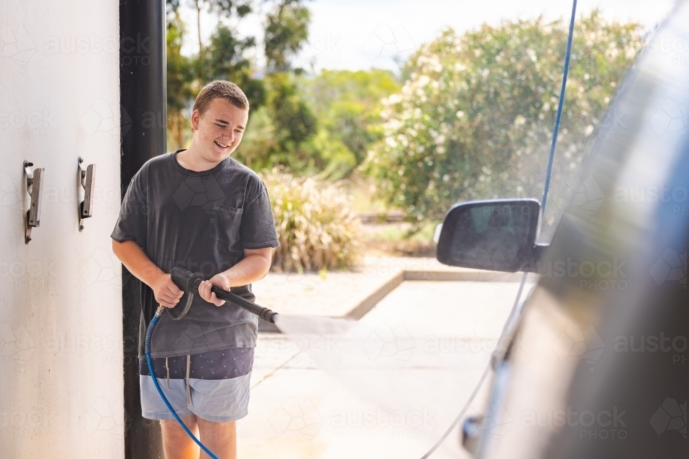 Teen boy washing vehicle in self-service car wash bay - Australian Stock Image