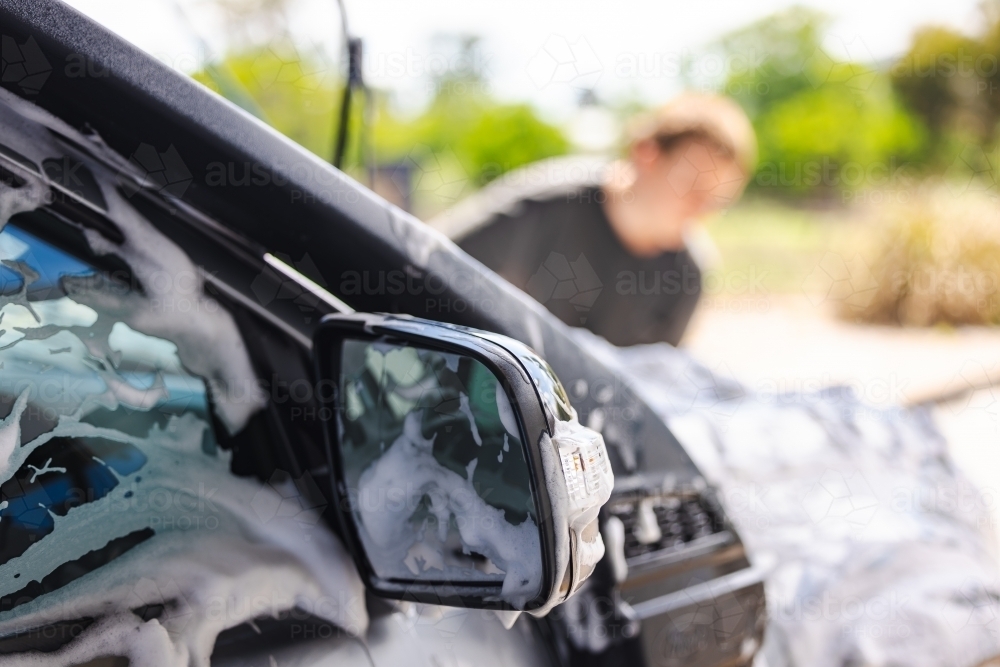 Teen boy washing vehicle in self-service car wash bay - Australian Stock Image