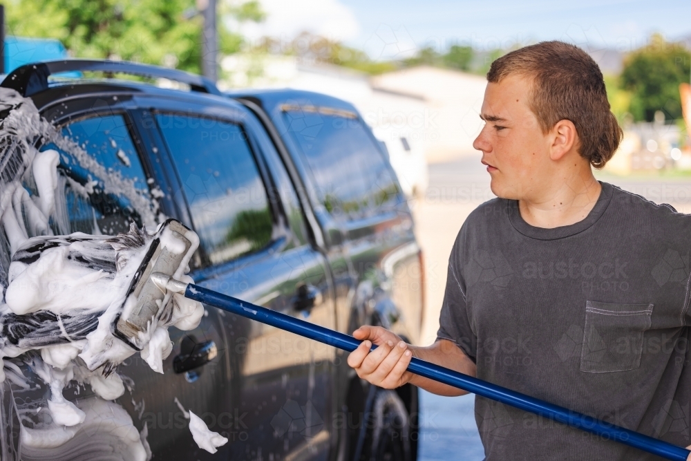 Teen boy washing vehicle in self-service car wash bay - Australian Stock Image