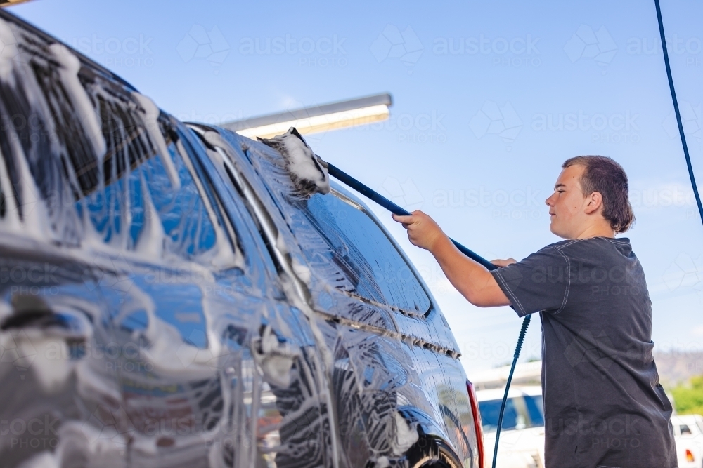 Teen boy washing vehicle in self-service car wash bay - Australian Stock Image