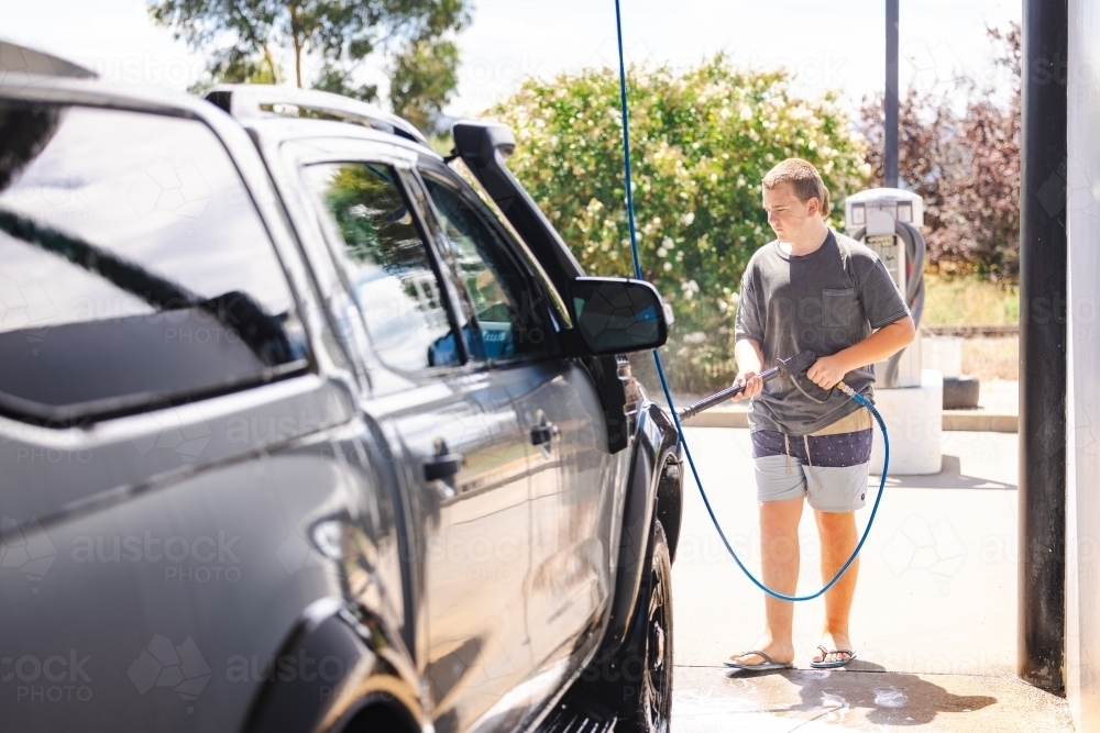 Teen boy washing vehicle in self-service car wash bay - Australian Stock Image