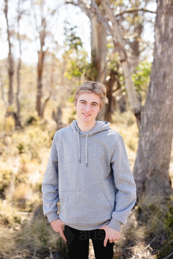 Teen boy wearing grey hoodie standing in bushland - Australian Stock Image