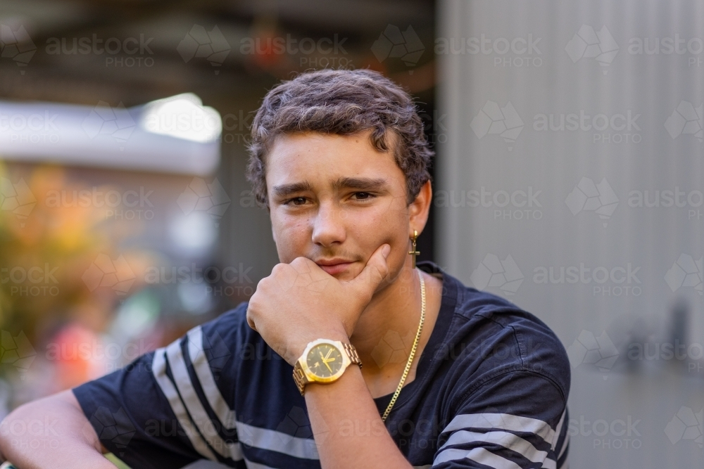teen boy wearing watched with hand on chin - Australian Stock Image