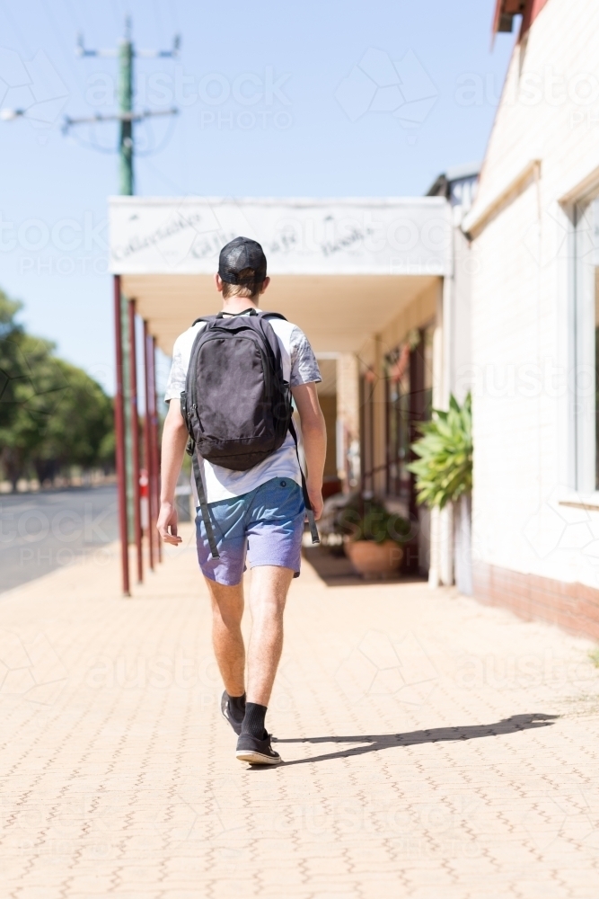 Teen boy with a backpack walking away on a footpath - Australian Stock Image
