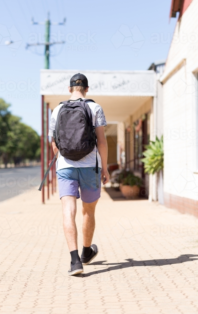 Teen boy with a backpack walking away on a footpath - Australian Stock Image