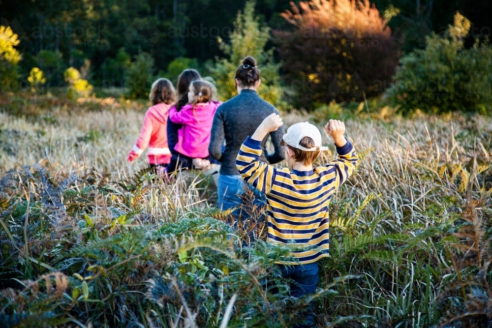 Teen cousins and younger siblings adventure through fern undergrowth in forest - Australian Stock Image