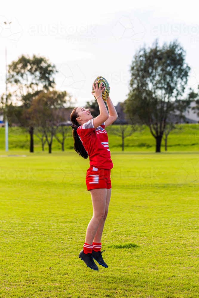 Teen footy player jumping to catch football ball during sports game - Australian Stock Image
