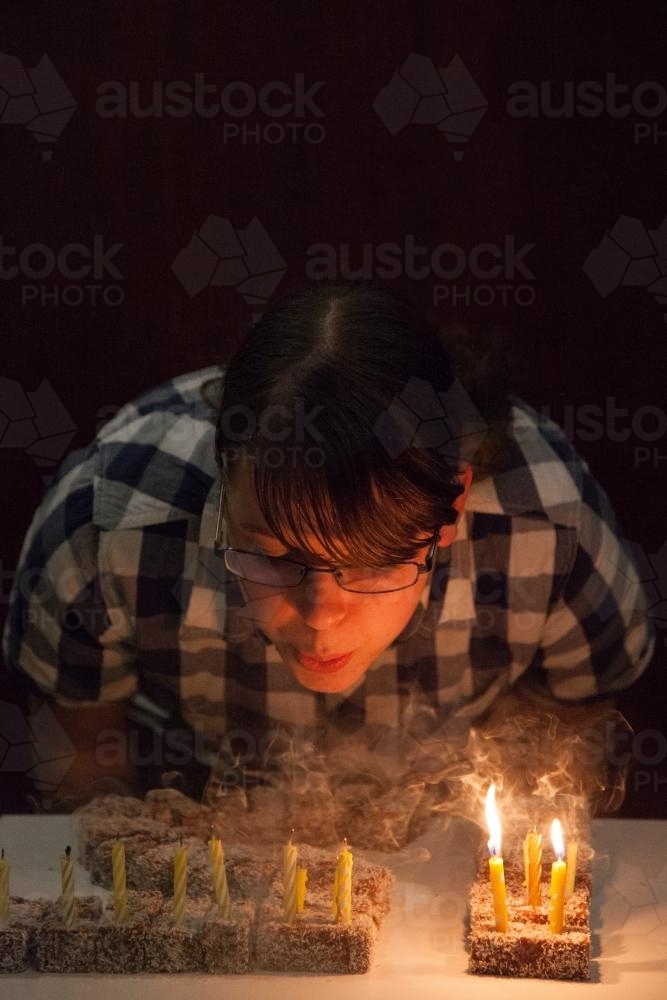 Teen girl blowing out fifteen candles on her lamington birthday cake - Australian Stock Image