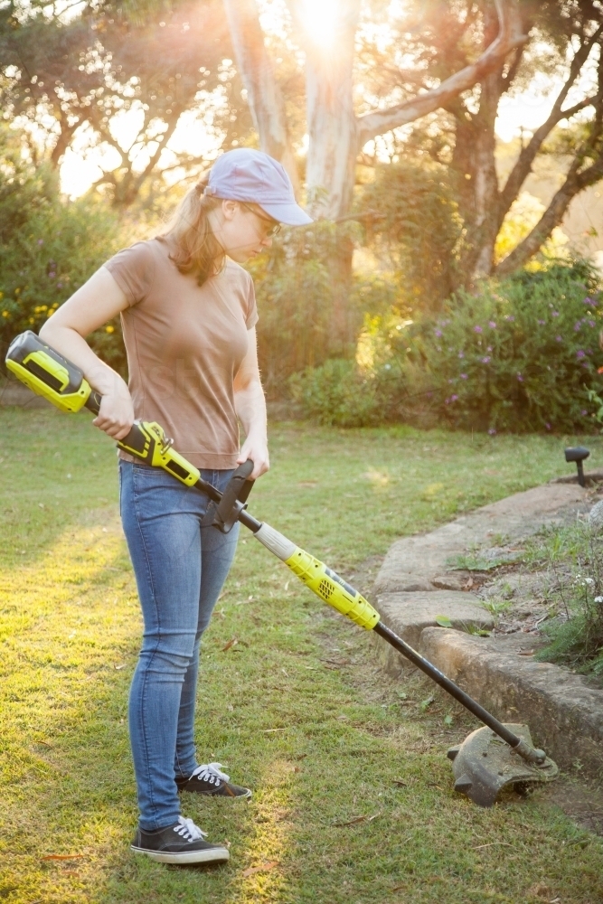 Image of Teen girl cutting grass with whipper snipper in golden