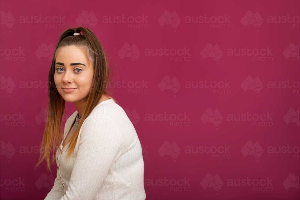 teen girl facing out of frame offset on dark pink background - Australian Stock Image