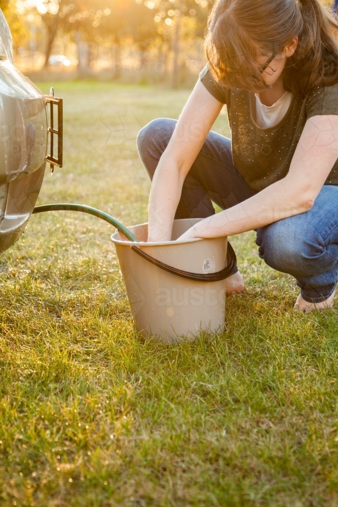 Teen girl filling up bucket of water for washing car - Australian Stock Image