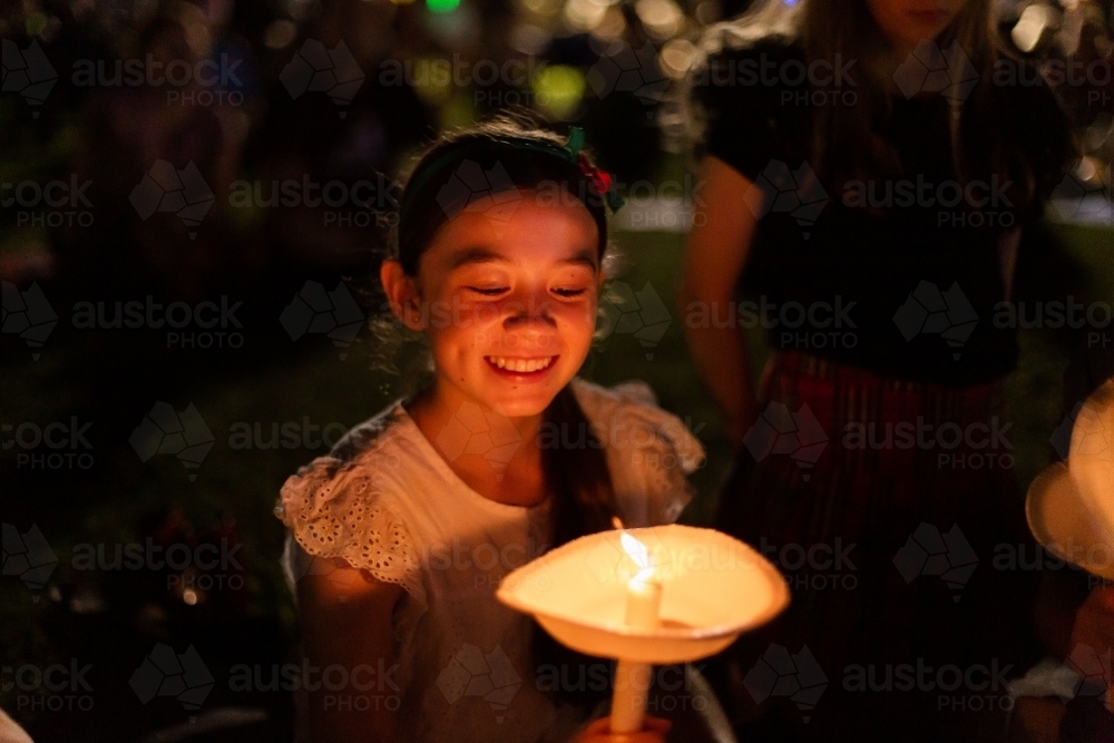 teen girl grinning and looking at her candle at carols by candlelight - Australian Stock Image