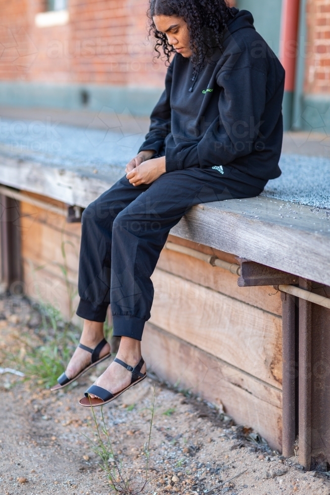 teen girl in black sitting on abandoned train station platform - Australian Stock Image