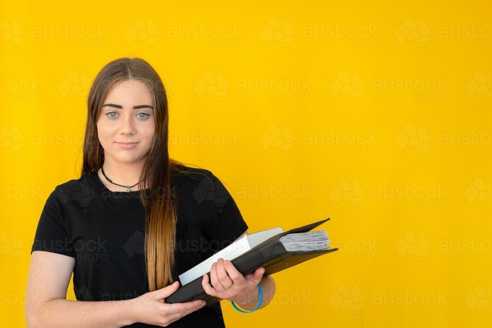 teen girl in black tee holding books against yellow background - Australian Stock Image