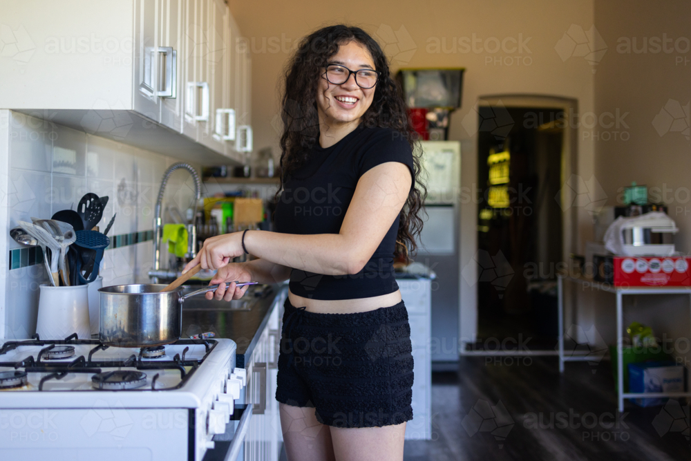 teen girl in kitchen stirring saucepan on stove - Australian Stock Image