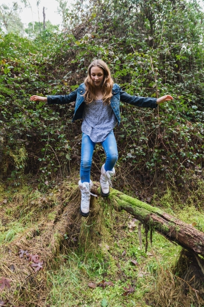 teen girl in motion, jumping off a log in a forest, some motion blur - Australian Stock Image