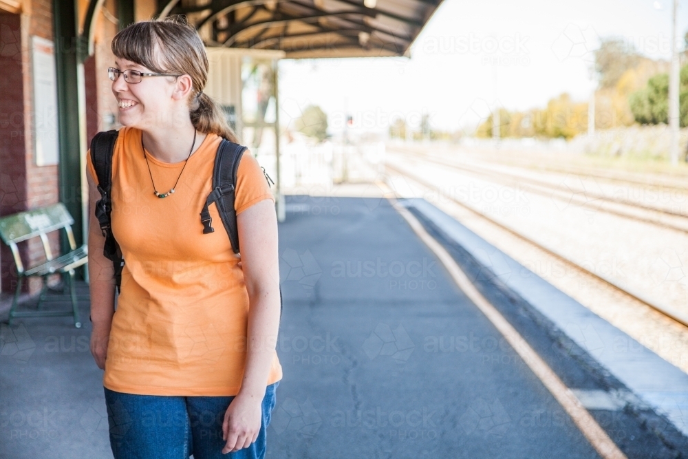 Teen girl in orange shirt with bag waiting at train station - Australian Stock Image
