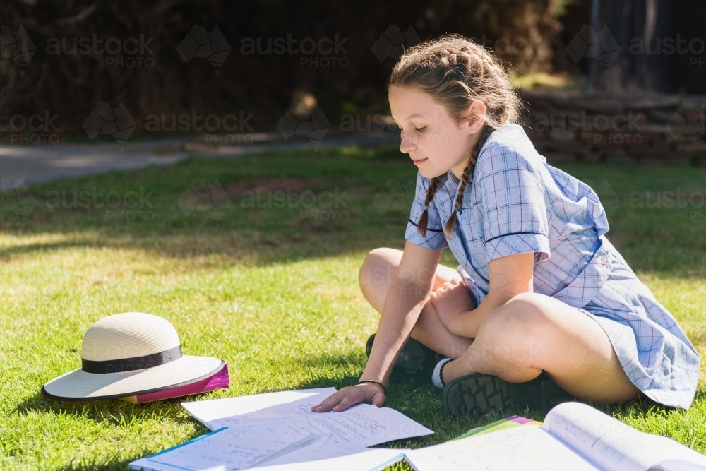 teen girl in school uniform doing homework outside on the grass - Australian Stock Image