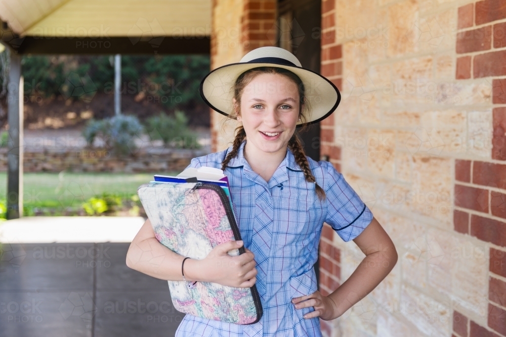 Teen girl in school uniform with books and laptop - Australian Stock Image