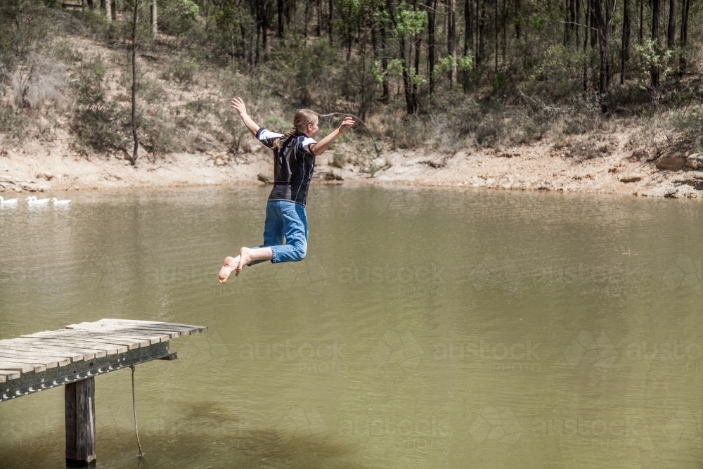 Teen girl jumping into a dam from the jetty - Australian Stock Image