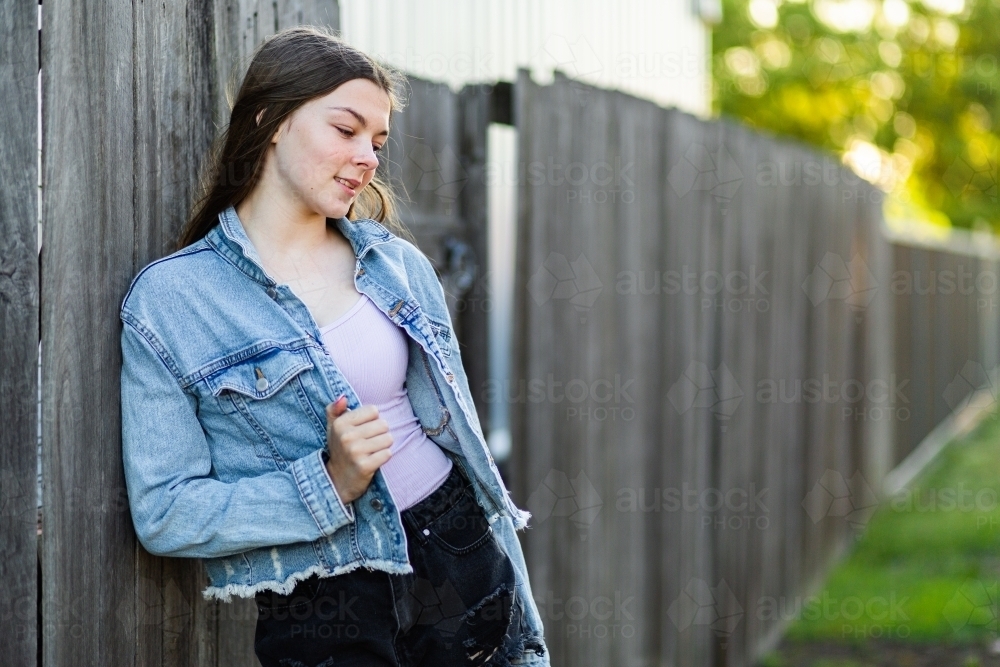 Teen girl leaning against a wooden fence looking down - Australian Stock Image
