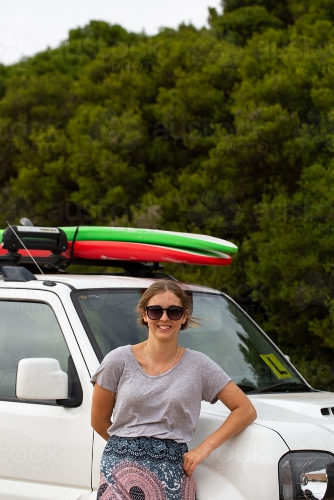 Teen girl leaning against suv with surfboards on roof rack - Australian Stock Image