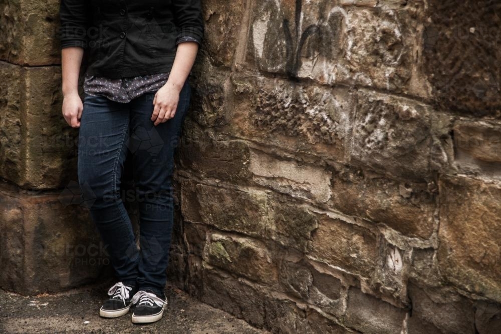 Teen girl leaning in corner on sandstone wall on an overcast day - Australian Stock Image