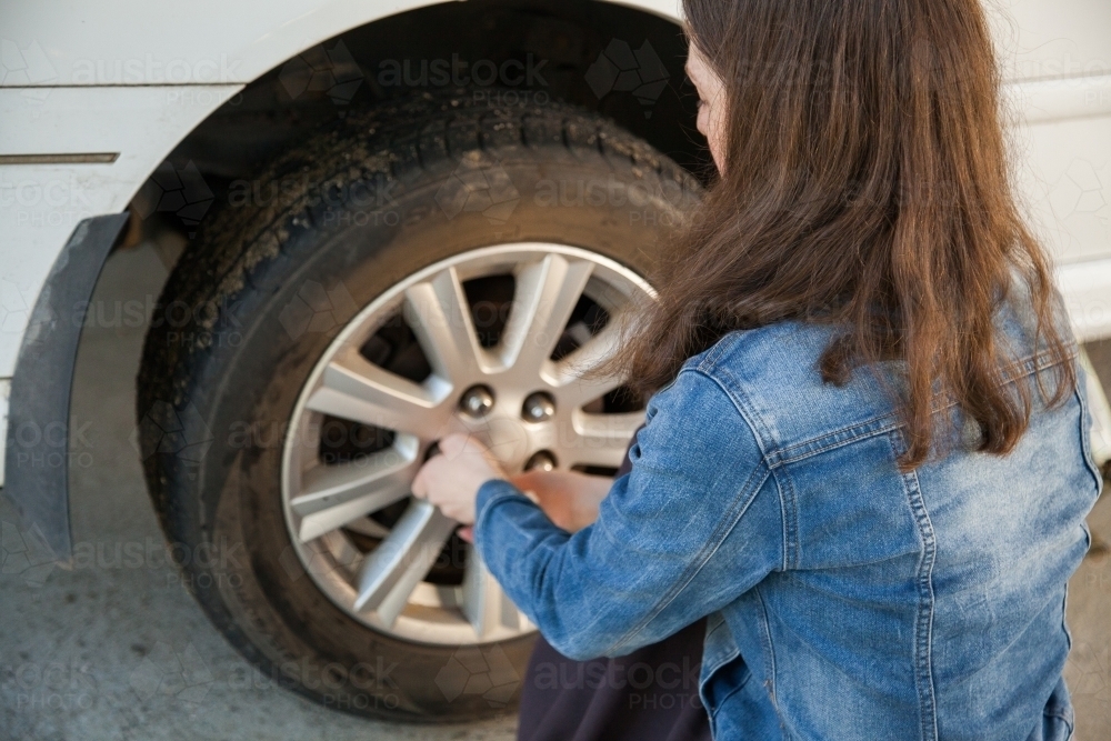 Teen girl learning how to change flat tyre unscrewing wheel nuts - Australian Stock Image