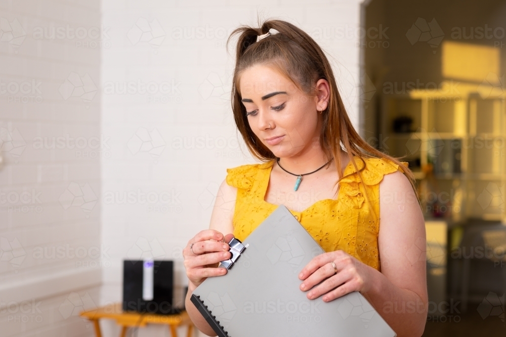 teen girl looking at folder she is holding in white room - Australian Stock Image