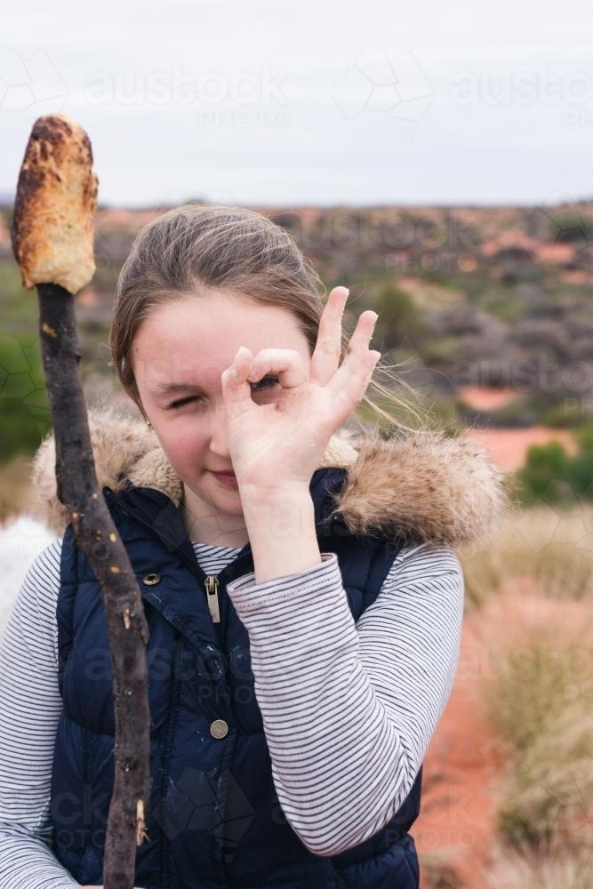Teen girl making a fun pose with her campfire bread, or Aussie damper - Australian Stock Image