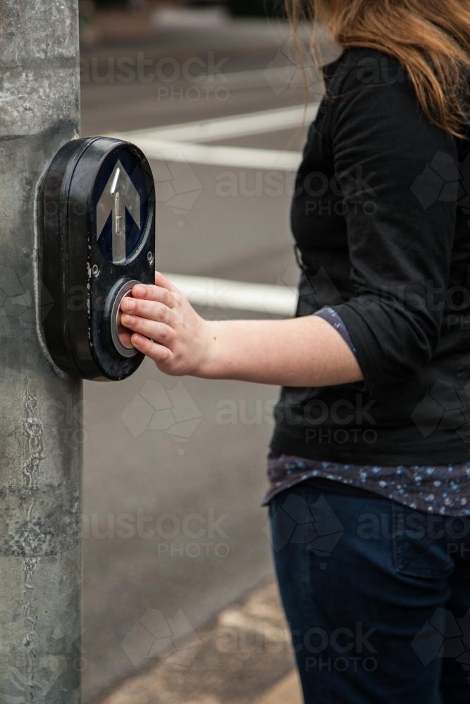 Teen girl pedestrian pressing the button at traffic lights street crossing - Australian Stock Image