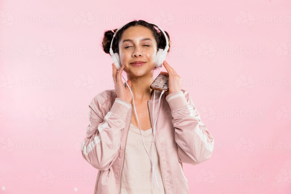 teen girl pin pink listening to music with headphones in studio - Australian Stock Image
