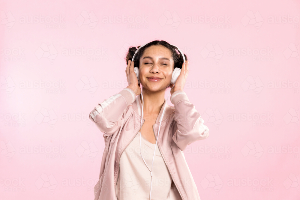teen girl pin pink listening to music with headphones in studio - Australian Stock Image