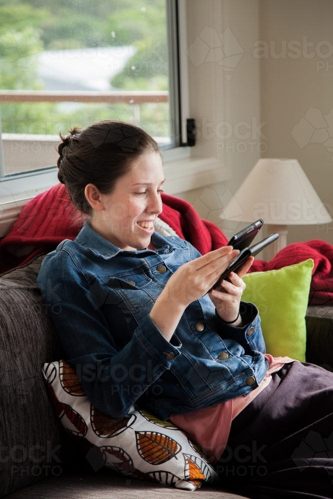 Teen girl reading book on tablet in lounge room - Australian Stock Image